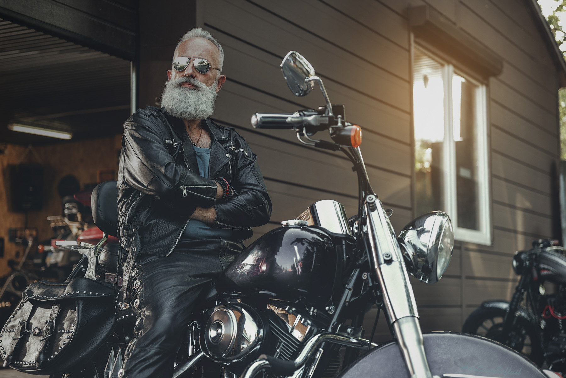 Concentrated aged biker in goggles is sitting at motorbike. He wearing leather jacket. Portrait. Low angle